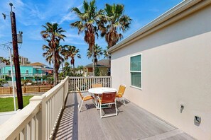 Un balcon avec une table et des chaises, donnant sur un quartier résidentiel bordé de palmiers et de maisons.
