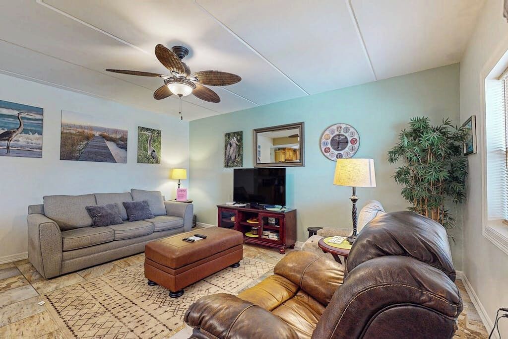 Un salon comprenant un canapé, un pouf et un fauteuil en cuir, un ventilateur de plafond, un téléviseur et des œuvres d’art murales.