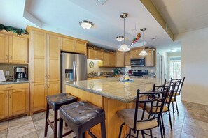 A kitchen with wooden cabinets, a stainless steel refrigerator, a large island with bar stools, and pendant lighting. - Ventura Condominiums #202 (South Padre Island)