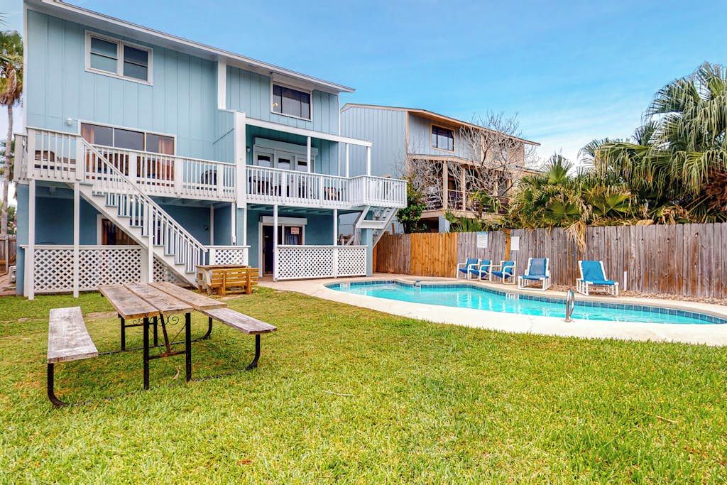 Uma casa de dois andares com piscina, deck de madeira e quintal cercado.