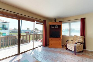 A room with a sliding glass door leading to a balcony, a wooden cabinet, and a patterned armchair. - Mezquite Duplex Beach House (South Padre Island)