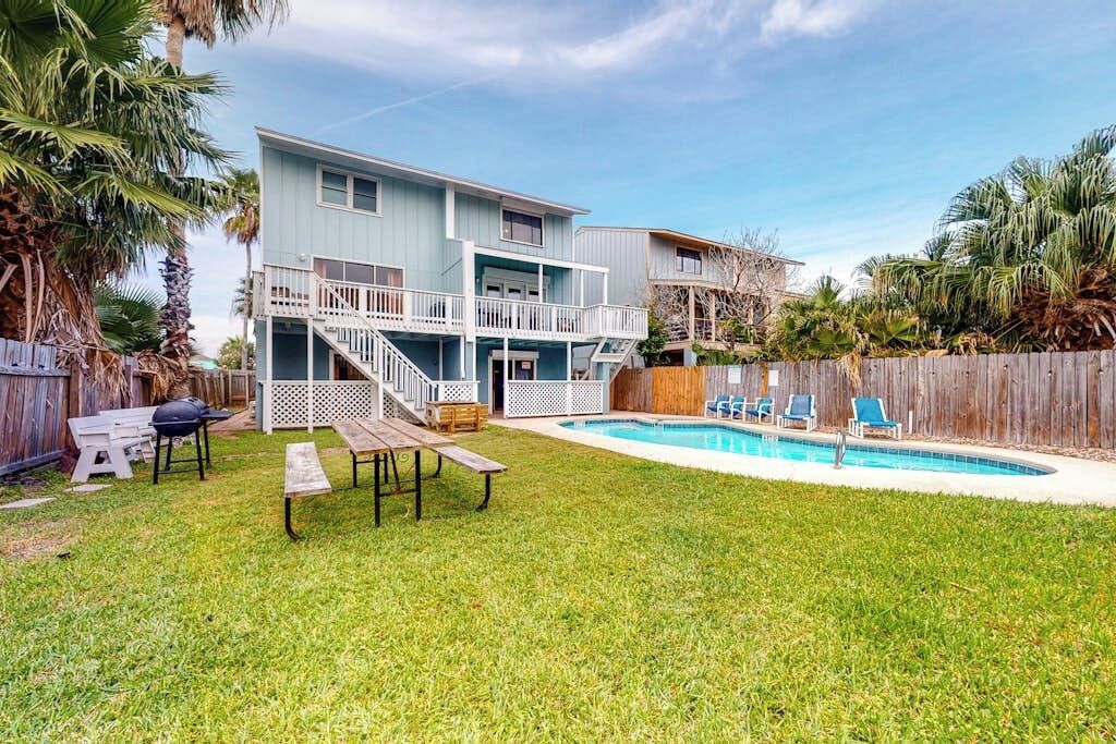 Uma casa de dois andares com piscina, deck de madeira e quintal cercado.