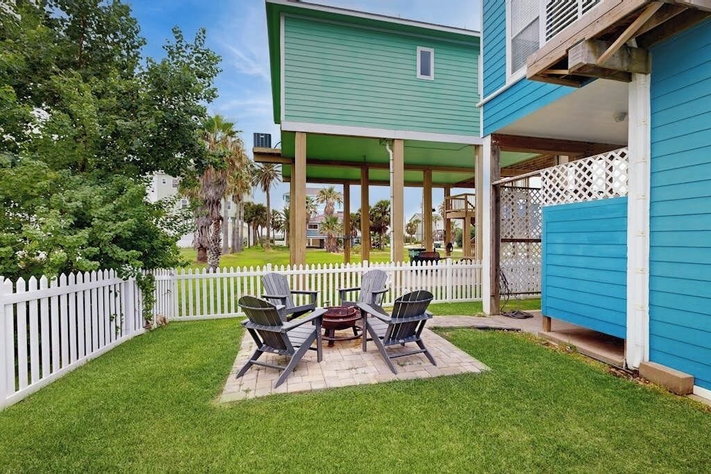 Ein grünes Haus mit überdachter Terrasse, weißem Zaun und Gartenmöbeln.
