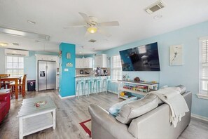 A modern kitchen with white cabinets, a stainless steel refrigerator, and a bar area with stools. - Beachwood - Fire Pit, Steps to Sand, Dogs OK (Galveston)