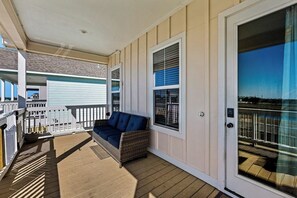 A covered outdoor area with a wicker sofa, a white railing, and a door leading to a balcony. - Just Peachie - Hot Tub, Yard & Steps to Sand (Galveston)