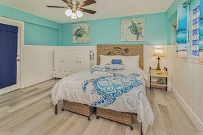 Ein Schlafzimmer mit einem Bett, einem Deckenventilator, Kunstwerken an den Wänden und einem Fenster mit Blick.