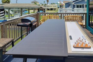 Eine Terrasse mit einem langen Tisch, Stühlen, einem Grill und einem Bowling-Set.