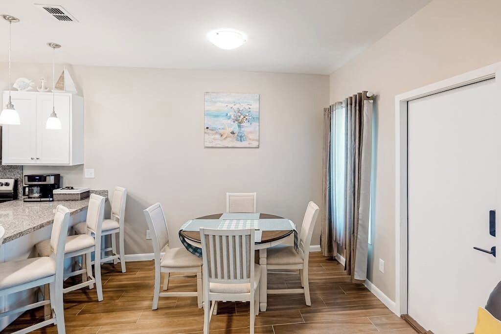 A dining area with a round table and chairs, a kitchen area with cabinets and appliances, and a painting on the wall.