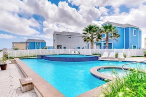 A swimming pool with a white fence, lounge chairs, and a building with blue siding. - Las Joyas Bayview Home #217 (Port Isabel)