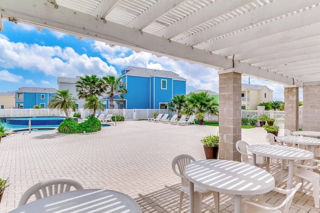 Un espace extérieur aménagé en terrasse, avec des chaises longues et des tables, une piscine, et un bâtiment bleu en arrière-plan.