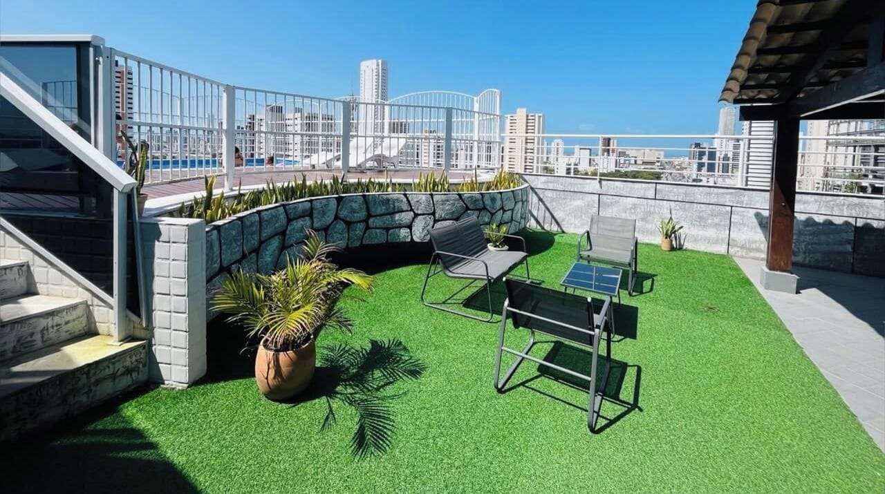 A rooftop terrace with artificial grass, a seating area, and a view of the city skyline.