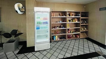 Hotellin aula, jossa on juomia sisältävä jääkaappi, seinällä peili ja hyllyllä pientä purtavaa.