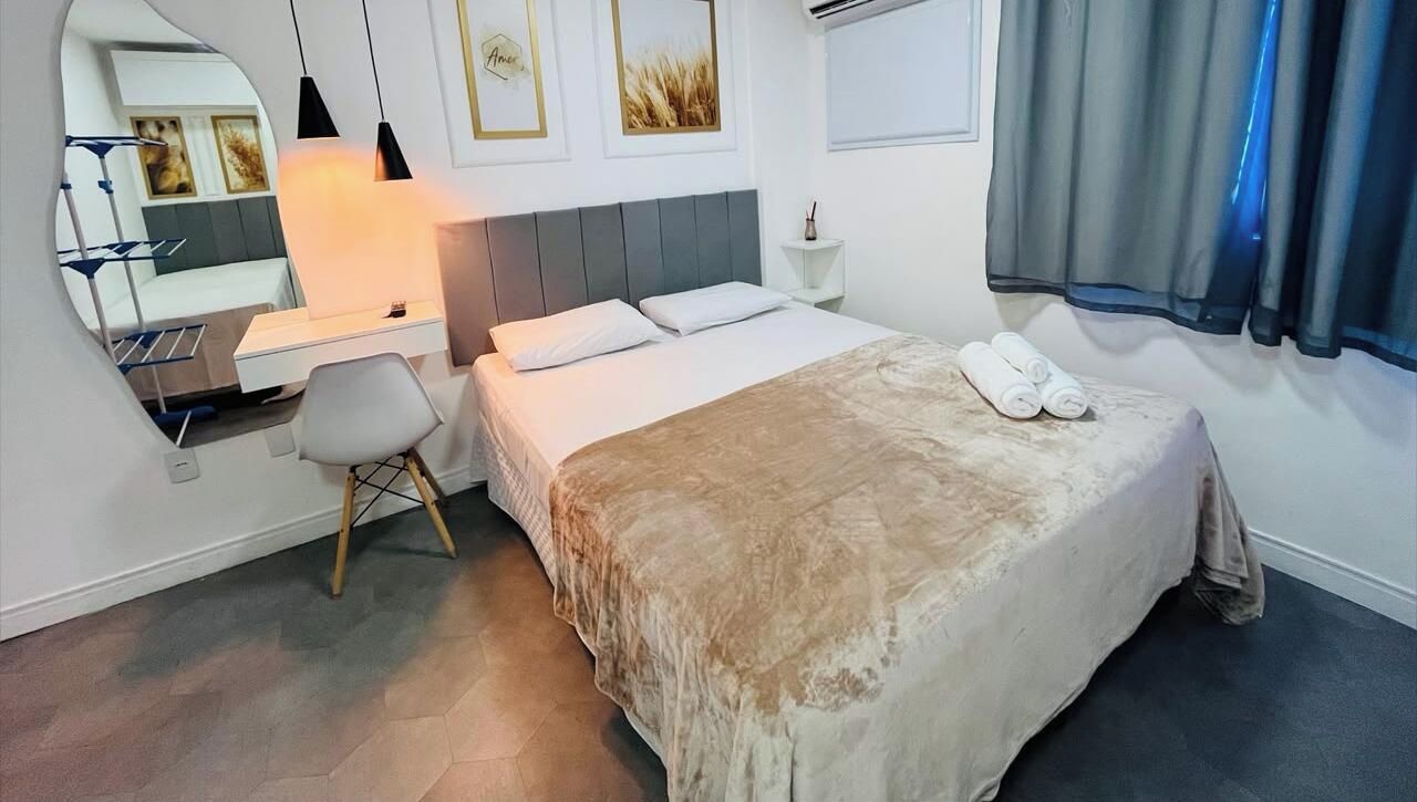 A modern hotel room with a bed, a desk, a chair, a mirror, and a window with curtains.