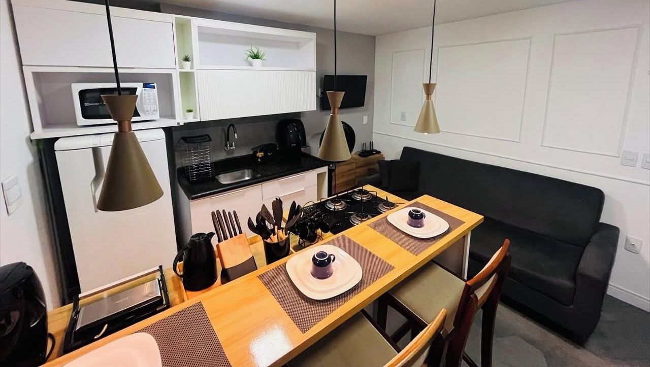 Cocina compacta con mesa de comedor, sillas y sofá negro.