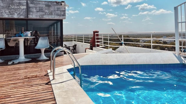 Una piscina sul tetto con un solarium in legno, un tavolo con sedie e vista sul paesaggio.