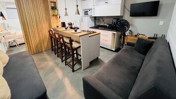 Cozinha moderna com ilha central, armários brancos e uma televisão de tela plana na parede.