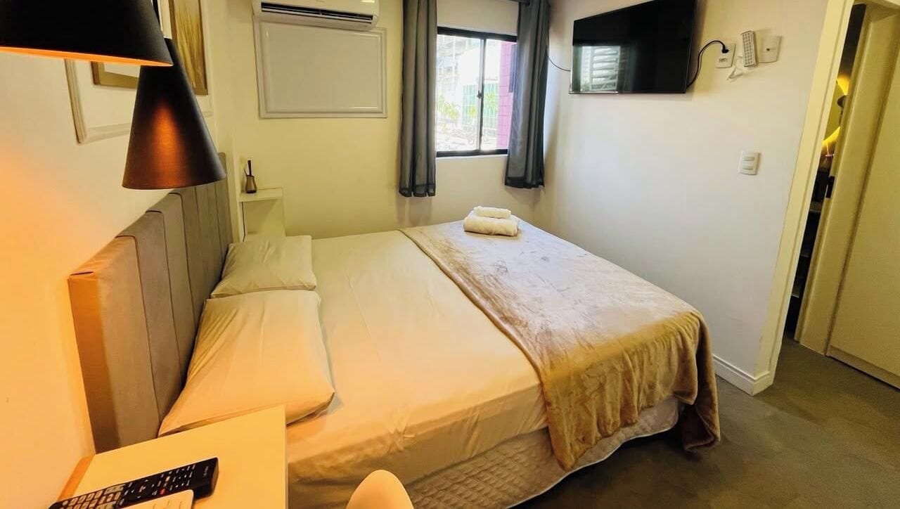 Una habitació d'hotel amb un llit, una taula de nit, una làmpada i un televisor penjat a la paret.