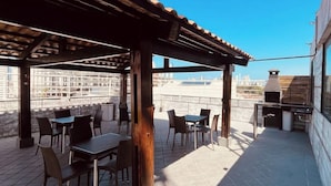 Una veranda esterna con tavoli e sedie, un pergolato e un barbecue.