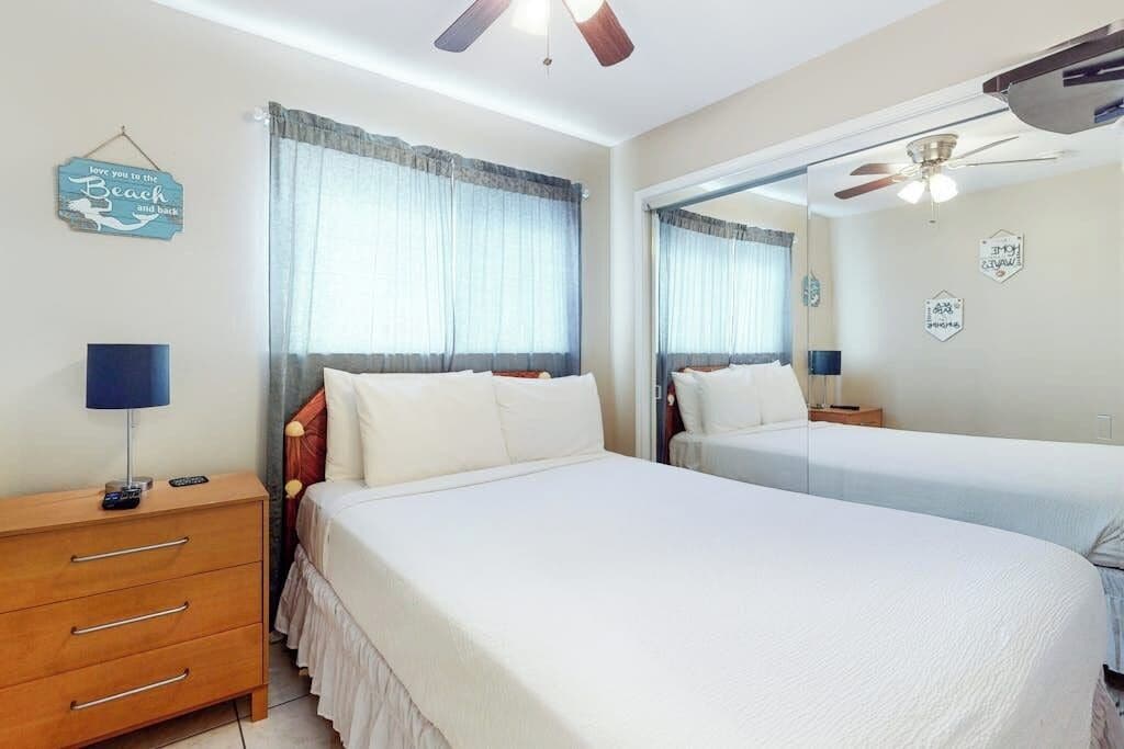 A hotel room with two beds, a wooden dresser, a mirror, and a ceiling fan.
