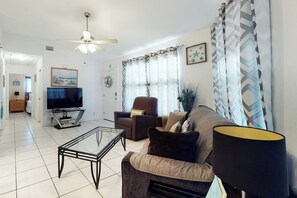 Un salon comprenant un canapé, un fauteuil, une table basse, un téléviseur et des rideaux.