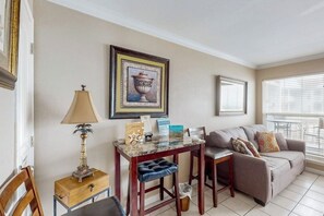 A living room with a sofa, a coffee table, a lamp, and framed artwork on the wall. - Curious Seagull - Heated Pool, Hot Tub & Balcony (Galveston)