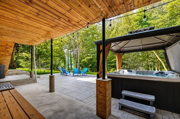An outdoor patio with a hot tub, wooden benches, and blue chairs.