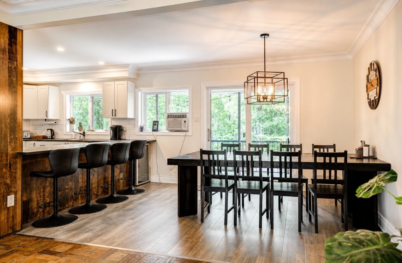 A modern kitchen with a bar area, wooden flooring, and large windows.