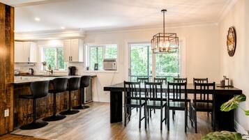 A modern kitchen with a bar area, wooden flooring, and large windows.