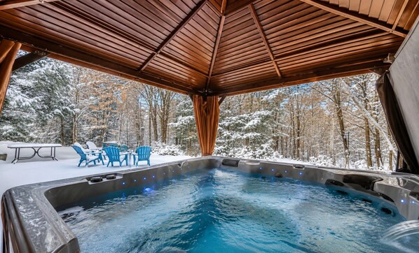 A hot tub with a wooden roof, surrounded by snow-covered trees.