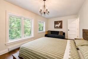 Un dormitorio con una cama grande, dos ventanas, una araña y un ciervo como decoración en la pared.