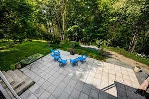 Un patio con sillas azules y una mesa, rodeado de un exuberante jardín y árboles.