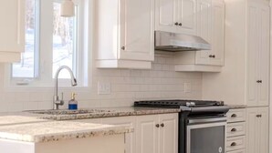 A kitchen with white cabinetry, a stainless steel range hood, a built-in oven, and a granite countertop. - Villa Belvédère |Vue panoramique et Nature ! (Grenville-Sur-La-Rouge)