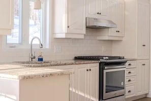 Una cocina con armarios blancos, una campana extractora de acero inoxidable, un horno empotrado y una encimera de granito.