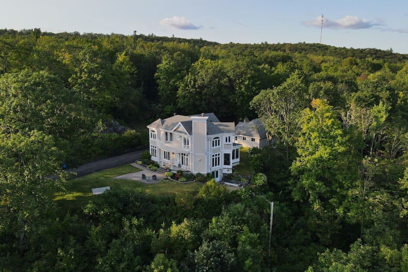 Une grande maison à deux étages, dotée d’un porche avant imposant et de nombreuses fenêtres, entourée d’une forêt dense.