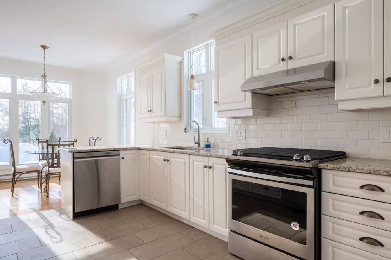 A kitchen with white cabinets, a stainless steel dishwasher, a double oven, and a granite countertop.