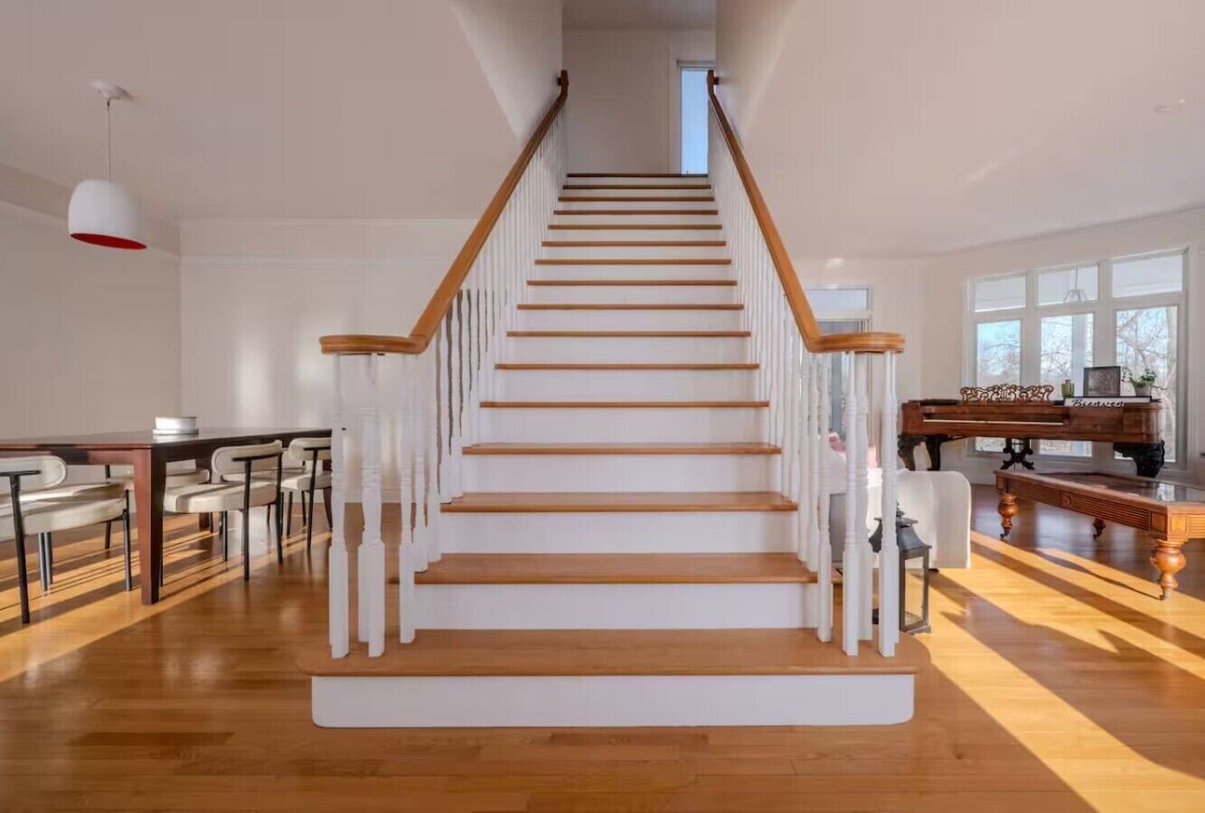 Un escalier avec des marches en bois et des balustrades blanches, menant à un palier où se trouve un piano.