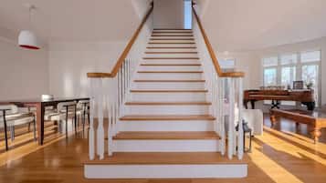 Un escalier avec des marches en bois et des balustrades blanches, menant à un palier où se trouve un piano.