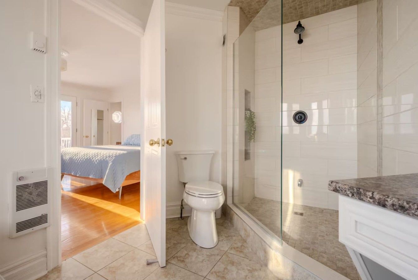 A bathroom with a glass shower enclosure, a toilet, and a sink with a marble countertop.