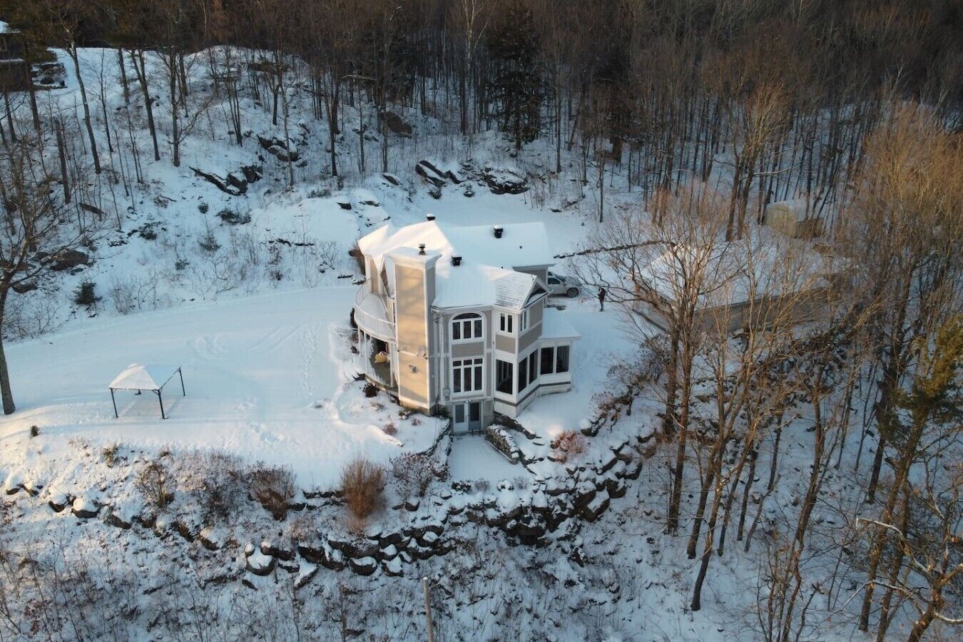 A snow-covered house with a large deck and a stone wall surrounding the property.