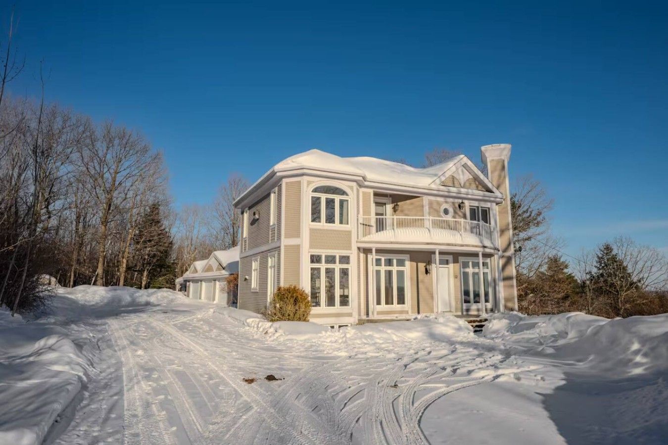A large, two-story house with a balcony, surrounded by snow-covered ground and trees.