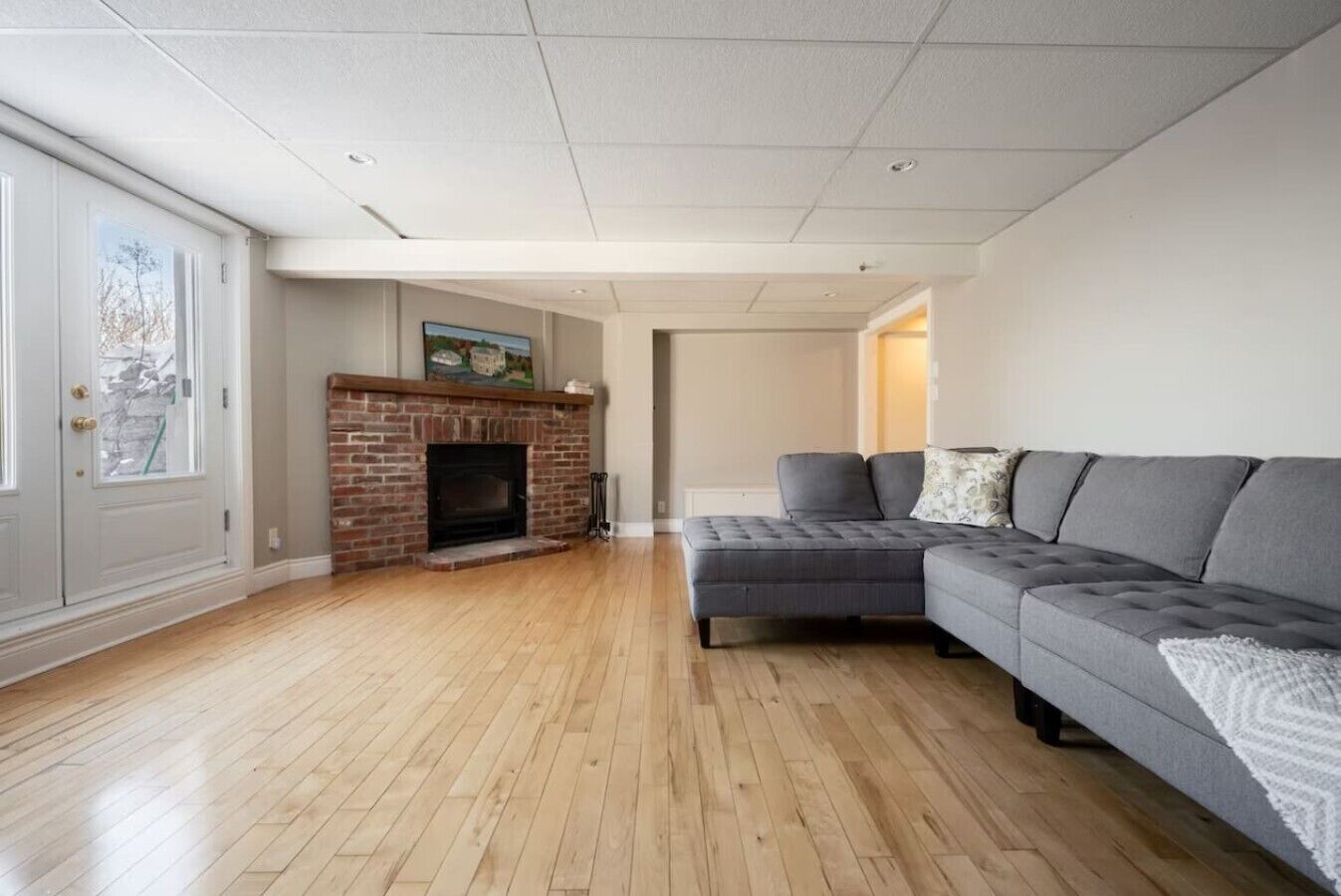 A living room with a fireplace, a grey sectional sofa, and hardwood flooring.