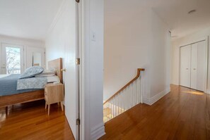 A bedroom with a wooden floor, a bed with a blue blanket, a nightstand, and a door leading to another room.