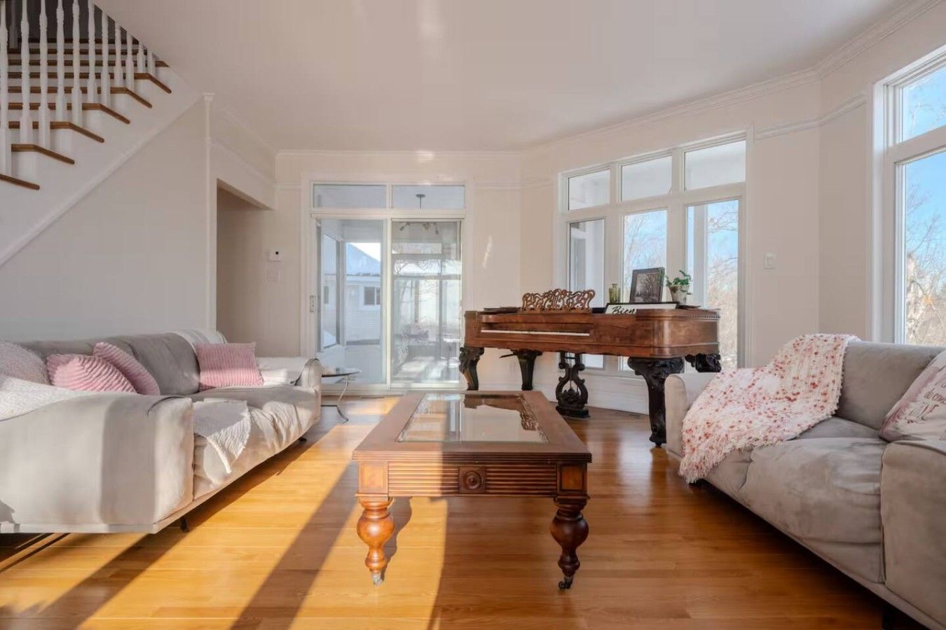 A spacious living room with a grand piano, two sofas, a coffee table, and a staircase.