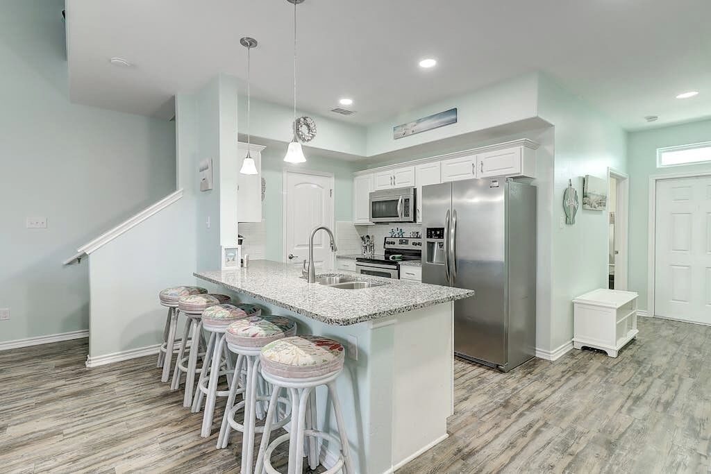 A kitchen with a central island, bar stools, stainless steel appliances, and a staircase leading to another level.