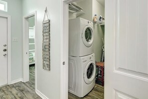 A laundry room with stacked washers and dryers, a hanging rack, and a door leading to a closet. - Nemo Cay - Nautical Nemo Cay (Corpus Christi)