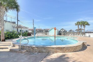 Una piscina circular con borde de ladrillo, rodeada de sillones de descanso y palmeras.