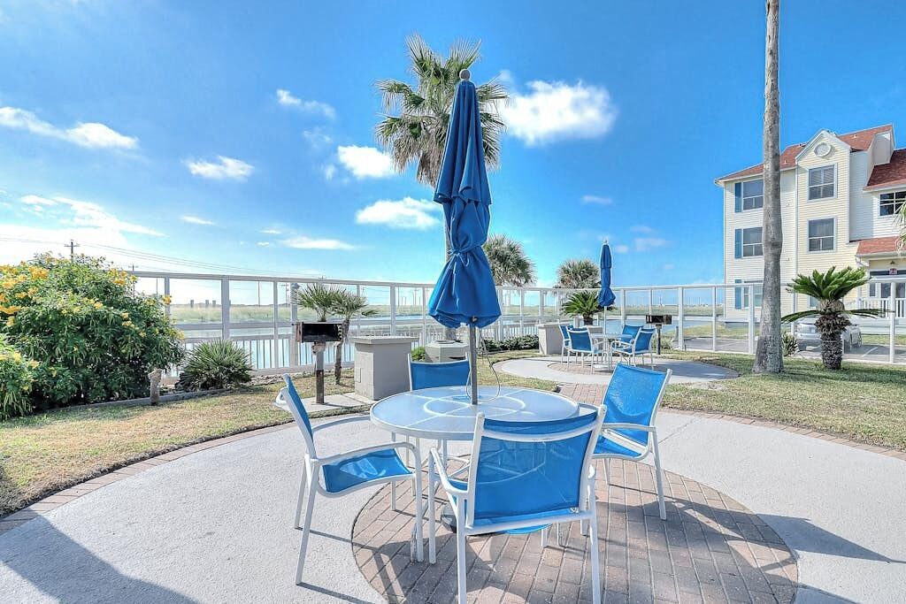 Een terras buiten met ronde tafels en stoelen, parasols en uitzicht op de oceaan.