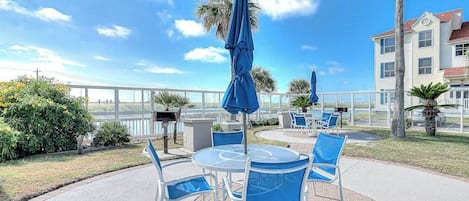 An outdoor patio area with round tables and chairs, umbrellas, and a view of the ocean.