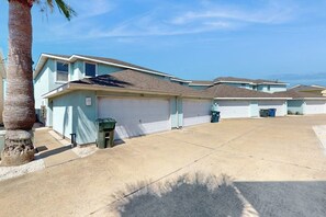 A residential area with light blue houses, a concrete driveway, and a palm tree. - Village Townhomes on the Greens Unit 106 (Corpus Christi)