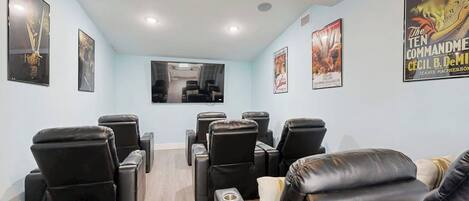 A movie theater with black leather reclining seats, a large screen, and posters on the walls.
